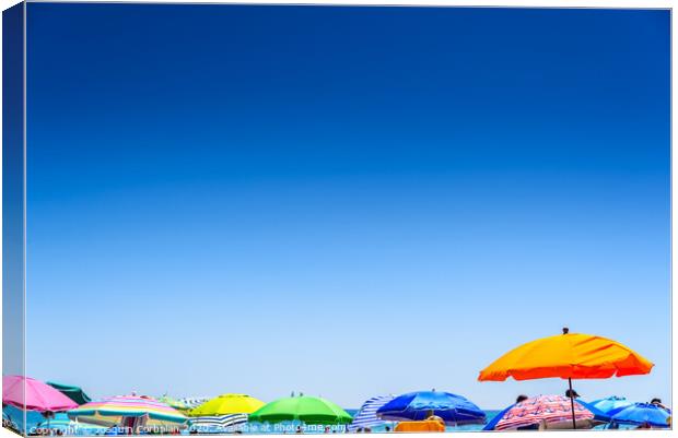 Colorful beach umbrella stuck in the sand surrounded by a group of bathers in summer, near the Mediterranean sea. Canvas Print by Joaquin Corbalan