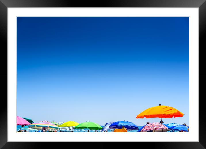 Colorful beach umbrella stuck in the sand surrounded by a group of bathers in summer, near the Mediterranean sea. Framed Mounted Print by Joaquin Corbalan