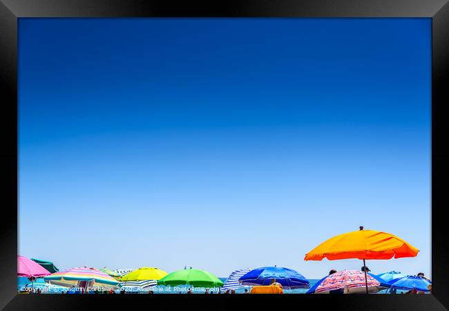 Colorful beach umbrella stuck in the sand surrounded by a group of bathers in summer, near the Mediterranean sea. Framed Print by Joaquin Corbalan