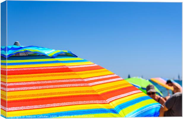 Colorful beach umbrella stuck in the sand surrounded by a group of bathers in summer, near the Mediterranean sea. Canvas Print by Joaquin Corbalan
