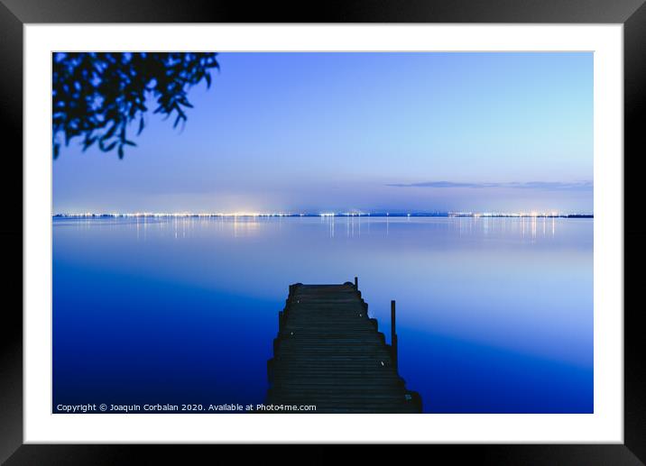 Pier on a lake at sunset with calm water and reflections of relaxing lights. Framed Mounted Print by Joaquin Corbalan