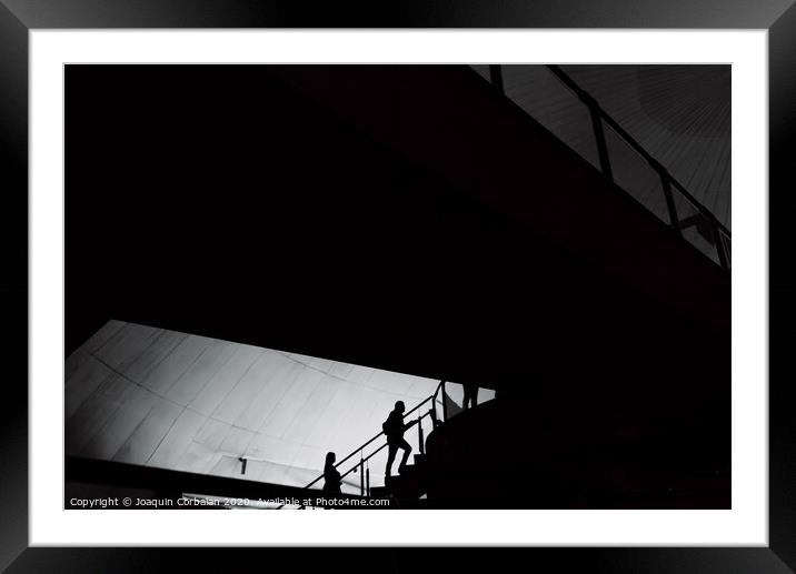 Silhouettes of people inside a building crossing stairs and walkways. Framed Mounted Print by Joaquin Corbalan