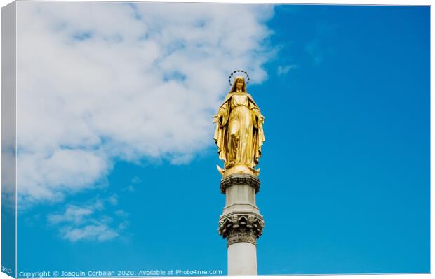 Golden religious statue, illuminated by the sun, of the Virgin Mary on top of a pedestal, with a background of blue sky and clouds. Canvas Print by Joaquin Corbalan