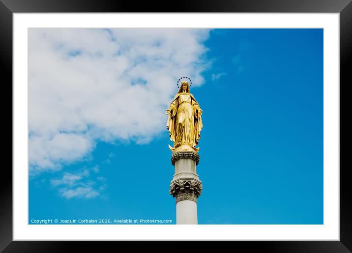 Golden religious statue, illuminated by the sun, of the Virgin Mary on top of a pedestal, with a background of blue sky and clouds. Framed Mounted Print by Joaquin Corbalan