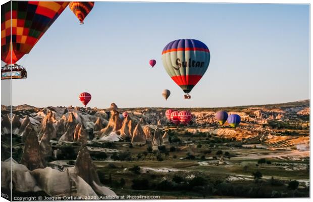 Travelers and tourists flying over mountains at sunset in a colorful aerostat balloon in Goreme, the Turkish cappadocia. Canvas Print by Joaquin Corbalan