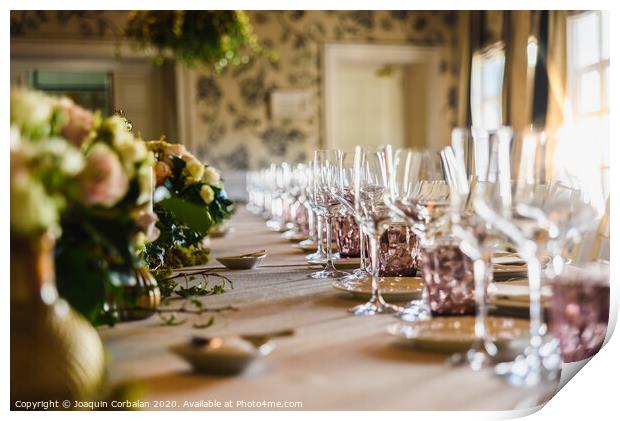 Elongated table with all the cutlery elegantly arranged and beautiful centerpieces ideal for decorating a wedding. Print by Joaquin Corbalan