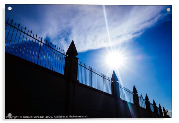 Silhouette against the sun of a high wall and metal fence with an intense blue sky in the background. Acrylic by Joaquin Corbalan