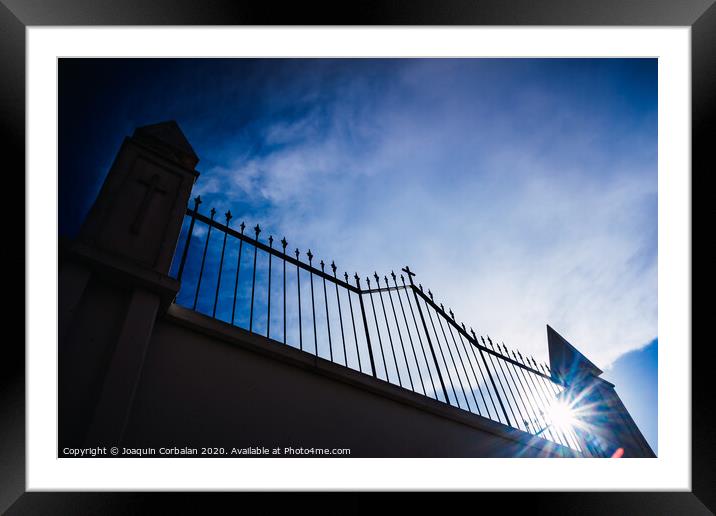 Metal grating of a cemetery with a cross on a white wall, copy space and deep and vibrant blue sky background. Framed Mounted Print by Joaquin Corbalan