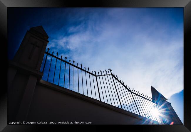Metal grating of a cemetery with a cross on a white wall, copy space and deep and vibrant blue sky background. Framed Print by Joaquin Corbalan