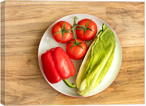 Bulgarian pepper, tomato and romaine lettuce lie close-up on a white round porcelain plate against the background of a wooden table Canvas Print by Sergii Petruk