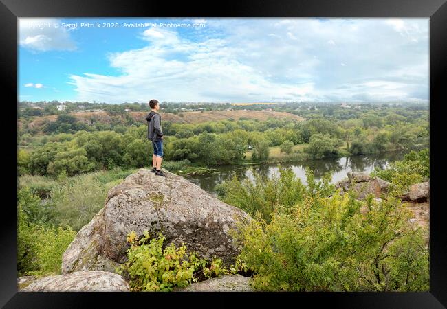 The teenager stands on top of a large stone boulder on the bank of the Southern Bug River and looks at the river below Framed Print by Sergii Petruk