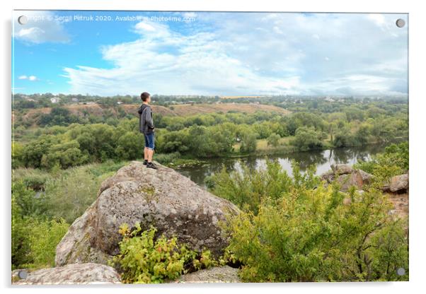The teenager stands on top of a large stone boulder on the bank of the Southern Bug River and looks at the river below Acrylic by Sergii Petruk