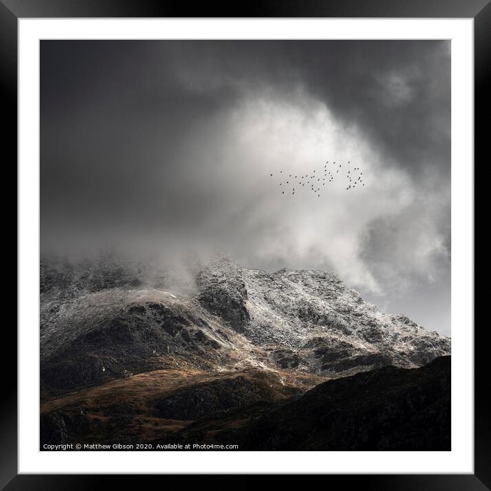 Stunning moody dramatic Winter landscape image of snowcapped Tryfan mountain in Snowdonia with stormy weather brooding overhead with birds flying high above Framed Mounted Print by Matthew Gibson