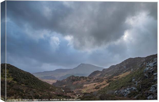 Moody and dramatic Winter landscape image of Moel Saibod from Crimpiau in Snowdonia with stunning shafts of light in stormy weather Canvas Print by Matthew Gibson
