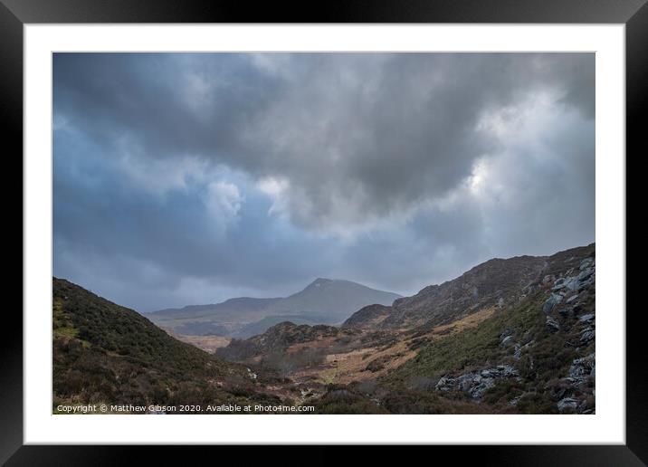 Moody and dramatic Winter landscape image of Moel Saibod from Crimpiau in Snowdonia with stunning shafts of light in stormy weather Framed Mounted Print by Matthew Gibson