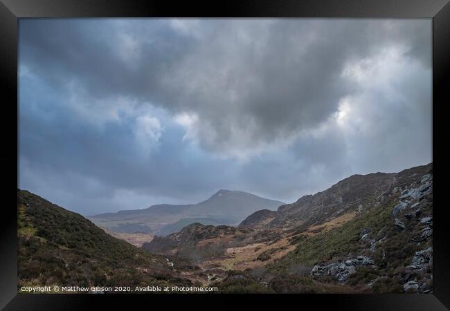 Moody and dramatic Winter landscape image of Moel Saibod from Crimpiau in Snowdonia with stunning shafts of light in stormy weather Framed Print by Matthew Gibson