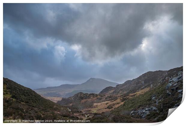 Moody and dramatic Winter landscape image of Moel Saibod from Crimpiau in Snowdonia with stunning shafts of light in stormy weather Print by Matthew Gibson