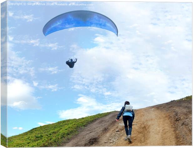 A young woman climbs up a mountain to meet a paraglider hovering in the air Canvas Print by Sergii Petruk
