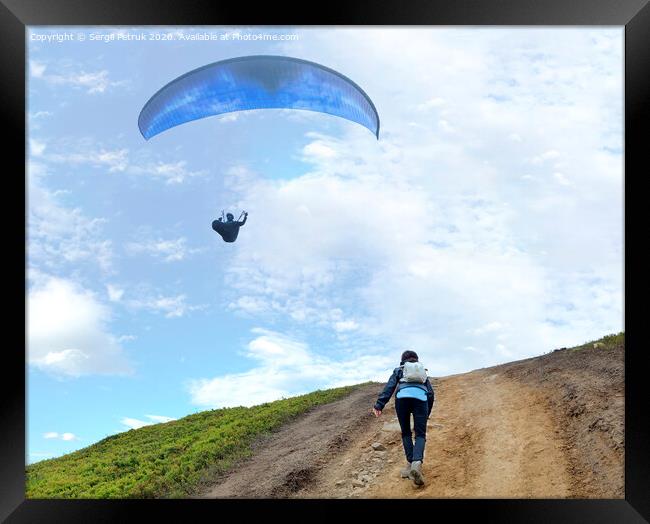 A young woman climbs up a mountain to meet a paraglider hovering in the air Framed Print by Sergii Petruk