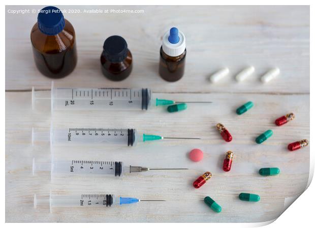 Syringes and capsules, medical ampoules and tablets on a white wooden table. Print by Sergii Petruk