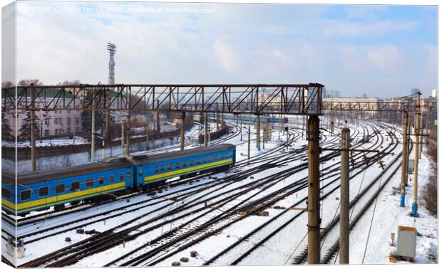 Passenger railway wagons ride along the railway tracks in the winter season against the backdrop of the cityscape Canvas Print by Sergii Petruk