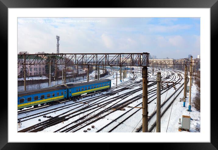 Passenger railway wagons ride along the railway tracks in the winter season against the backdrop of the cityscape Framed Mounted Print by Sergii Petruk