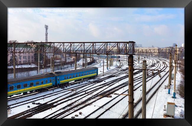 Passenger railway wagons ride along the railway tracks in the winter season against the backdrop of the cityscape Framed Print by Sergii Petruk