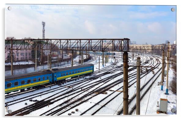 Passenger railway wagons ride along the railway tracks in the winter season against the backdrop of the cityscape Acrylic by Sergii Petruk