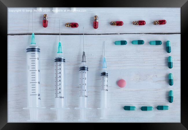 Medical syringes, capsules, pills lie vertically on a white roughly painted wooden table. Framed Print by Sergii Petruk