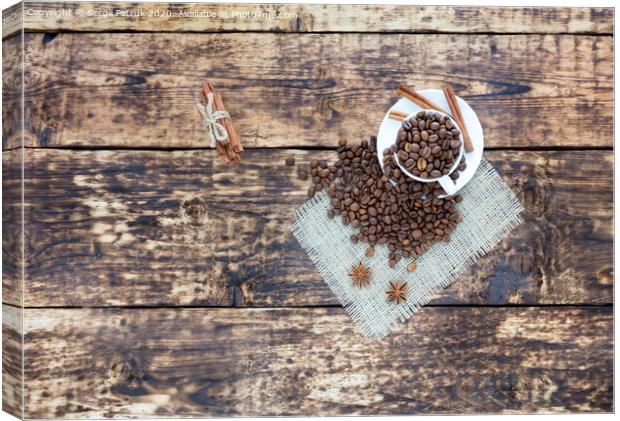 Grain coffee in a cup, which stands on a sackcloth from burlap. Cinnamon on a platter and tied with a rope. Anise stars complement the aroma of coffee. View from above. Canvas Print by Sergii Petruk