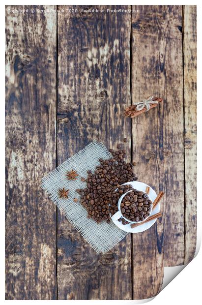 Grain coffee in a cup, which stands on a sackcloth from burlap. Cinnamon on a platter and tied with a rope. Anise stars complement the aroma of coffee. View from above. Print by Sergii Petruk