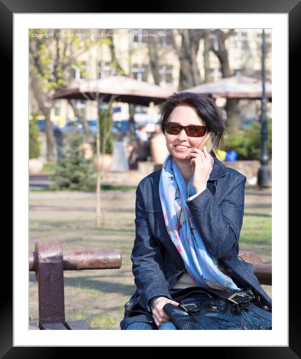 A young woman with a joyful mood communicates on a smartphone in a spring park Framed Mounted Print by Sergii Petruk