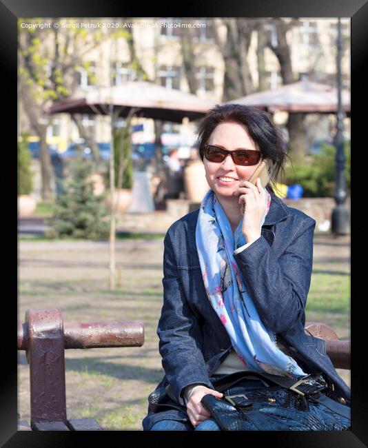 A young woman with a joyful mood communicates on a smartphone in a spring park Framed Print by Sergii Petruk