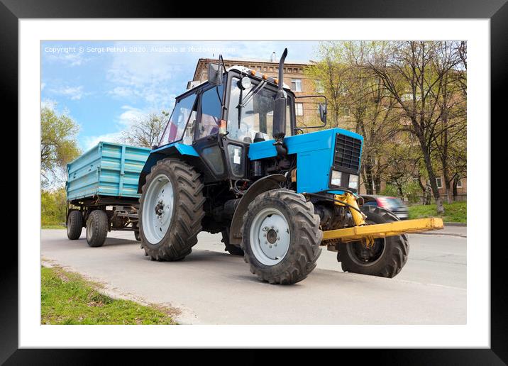 An old small blue tractor with a trailer stands on the side of the road Framed Mounted Print by Sergii Petruk