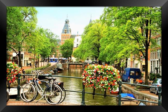 A bicycle parked on the side of a river in Amsterd Framed Print by M. J. Photography