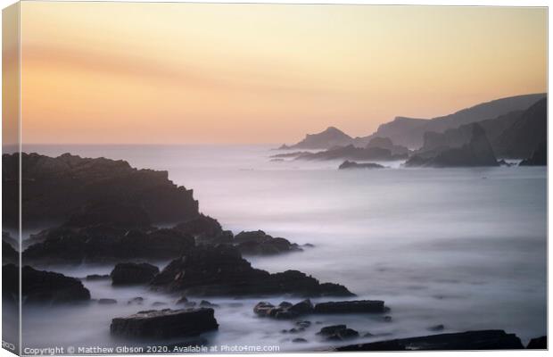 Beautiful long exposure landscape image of sea over rocks during vibrant sunset Canvas Print by Matthew Gibson