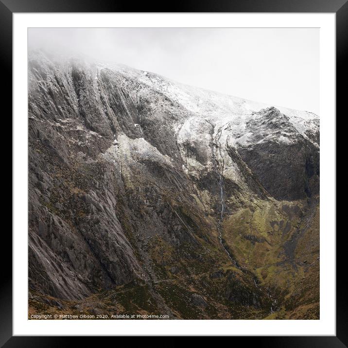 Stunning dramatic landscape image of snowcapped Glyders mountain range in Snowdonia during Winter with menacing low clouds hanging at the peaks Framed Mounted Print by Matthew Gibson