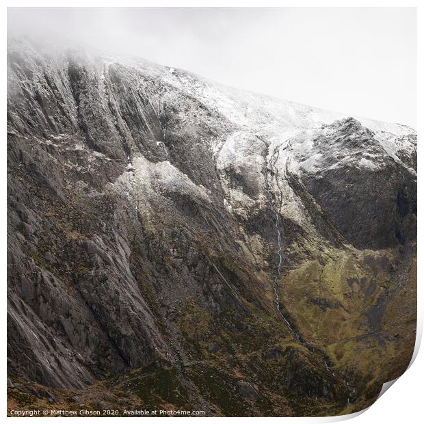 Stunning dramatic landscape image of snowcapped Glyders mountain range in Snowdonia during Winter with menacing low clouds hanging at the peaks Print by Matthew Gibson