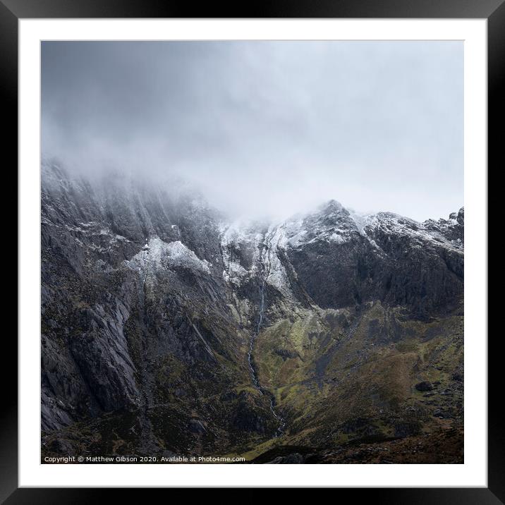 Stunning dramatic landscape image of snowcapped Glyders mountain range in Snowdonia during Winter with menacing low clouds hanging at the peaks Framed Mounted Print by Matthew Gibson