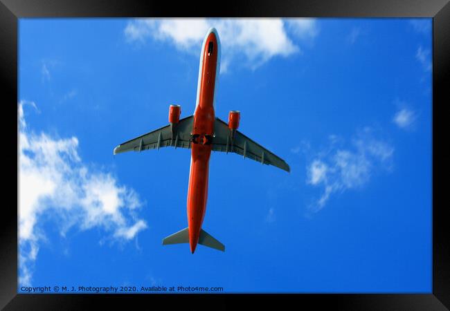 Passenger red airplane in the clouds and blue sky. Framed Print by M. J. Photography