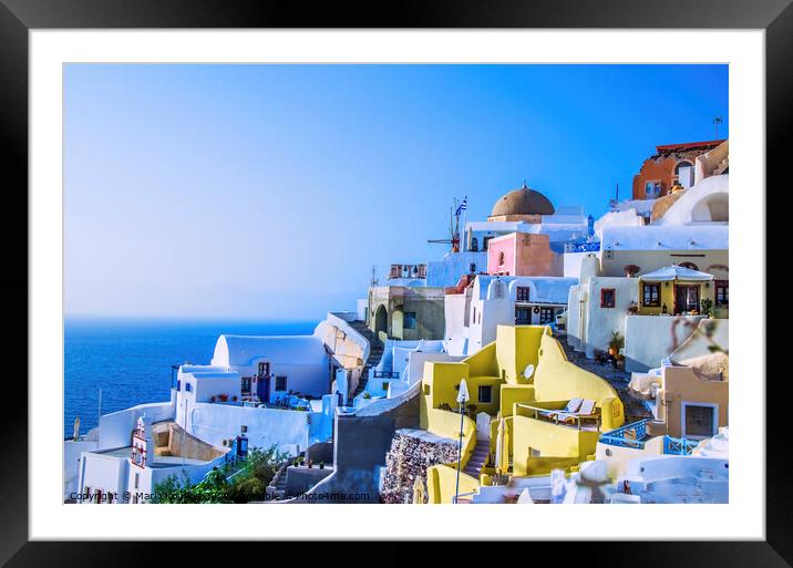 At dusk the sun bathes the traditional and colorful Greek houses in the town of Oia Framed Mounted Print by Mario Koufios