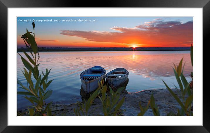 Two boats stand at the shore of a calm river against the background of a bright rising sun Framed Mounted Print by Sergii Petruk