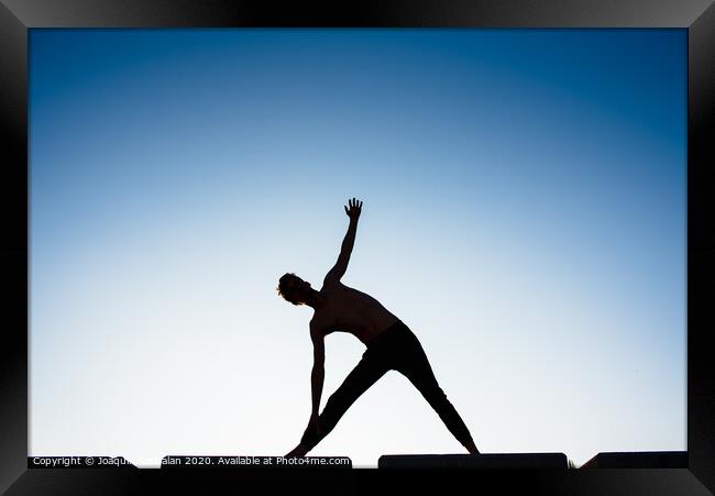 Silhouette of a man practicing yoga, isolated against the blue sky. Framed Print by Joaquin Corbalan