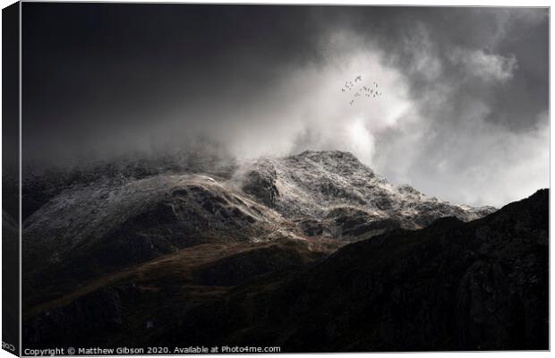 Stunning moody dramatic Winter landscape image of snowcapped Tryfan mountain in Snowdonia with stormy weather brooding overhead with birds flying high above Canvas Print by Matthew Gibson