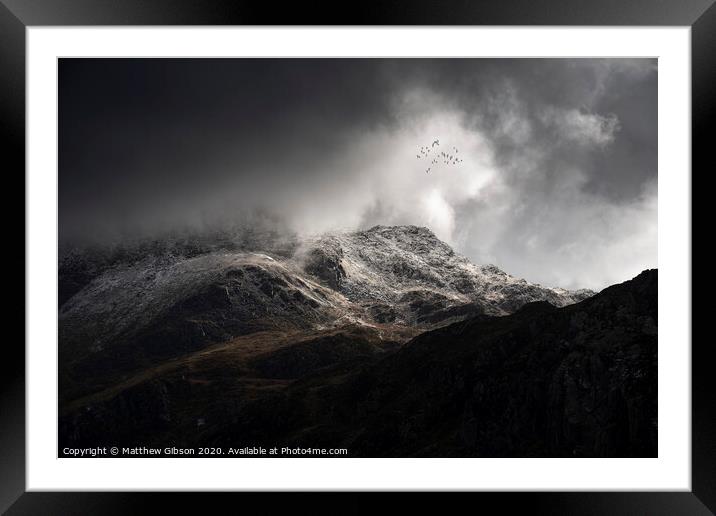Stunning moody dramatic Winter landscape image of snowcapped Tryfan mountain in Snowdonia with stormy weather brooding overhead with birds flying high above Framed Mounted Print by Matthew Gibson