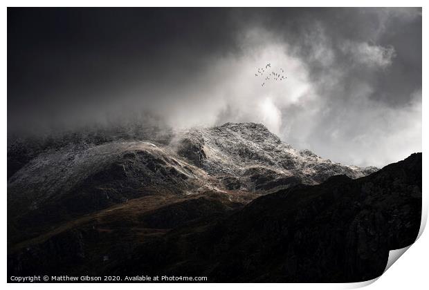 Stunning moody dramatic Winter landscape image of snowcapped Tryfan mountain in Snowdonia with stormy weather brooding overhead with birds flying high above Print by Matthew Gibson