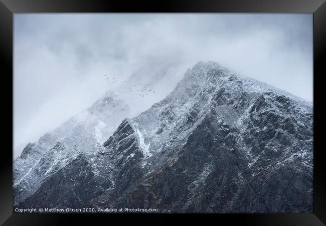 Stunning detail landscape images of snowcapped Pen Yr Ole Wen mountain in Snowdonia during dramatic moody Winter storm with birds flying high above Framed Print by Matthew Gibson