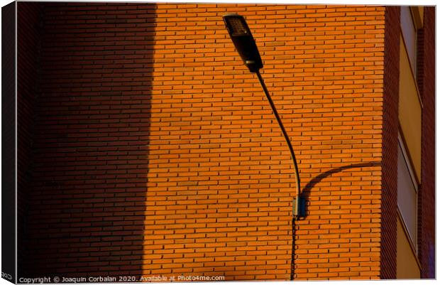 A deep red brick wall supports a lamppost, contrasting and bright colors. Canvas Print by Joaquin Corbalan