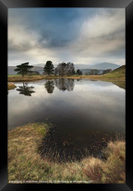 Stunning landscape image of dramatic storm clouds over Kelly Hall Tarn in Lake District during late Autumn Fall afternoon Framed Print by Matthew Gibson