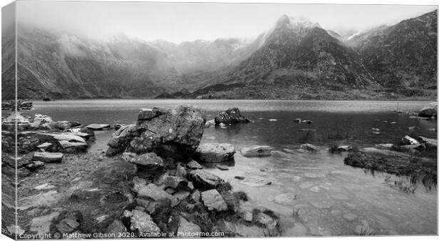 Beautiful moody Winter landscape image of Llyn Idwal and snowcapped Glyders Mountain Range in Snowdonia in black and white Canvas Print by Matthew Gibson
